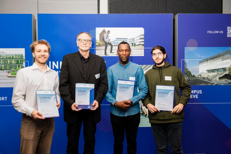 (v.l.): Gleb Byvaltsev (Mechatronic Systems Engineering, B.Sc.), Norbert Dewender (Dewender-Stiftung), Tanaka Mujaya (Industrial Engineering, B.Sc.) und Abbass Khraizat (Mechatronic Systems Engineering, B.Sc.).  Foto: Torsten Barthel (©Barthel Fotografie)